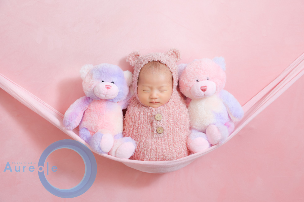 白い布の上で穏やかに眠る新生児と、優しく手を添える夫婦フォトグラファー。